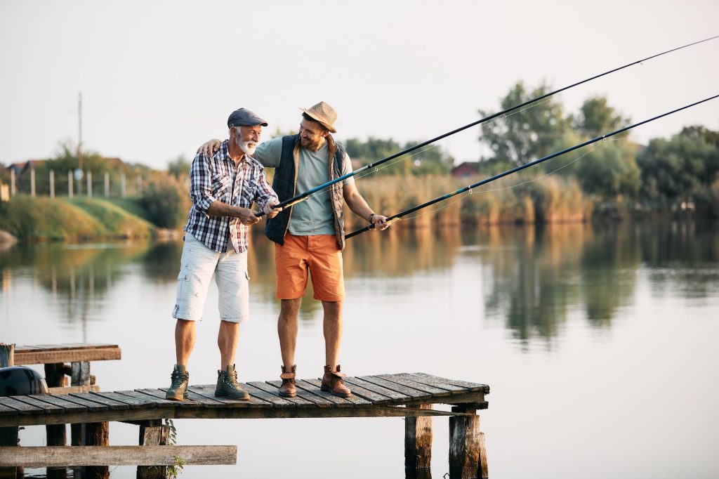 Happy mature man and his son enjoying while fishing from a pier.